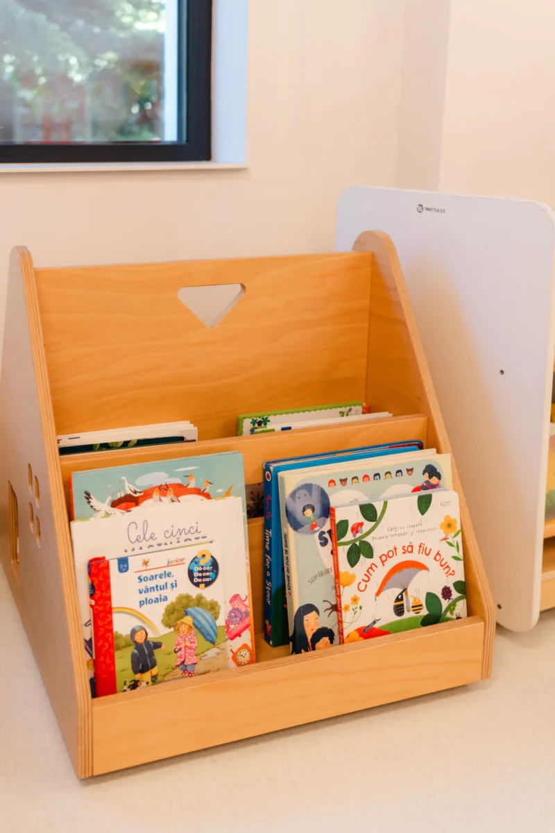 Raft de lemn cu cărți ilustrate pentru copii, la înălțimea lor, în centrul Bibliotecă de la Grădinița Amicus Junior din Iași