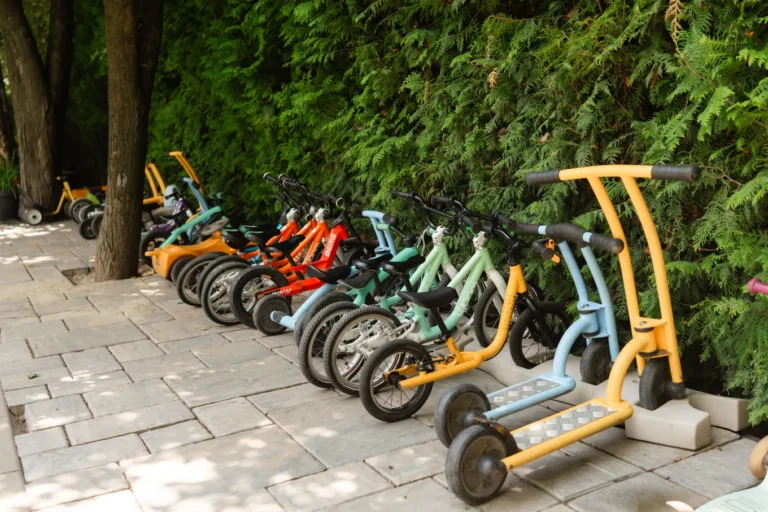 Biciclete fără pedale și trotinete aliniate pe aleea din curtea Grădiniței Amicus Junior din Iași