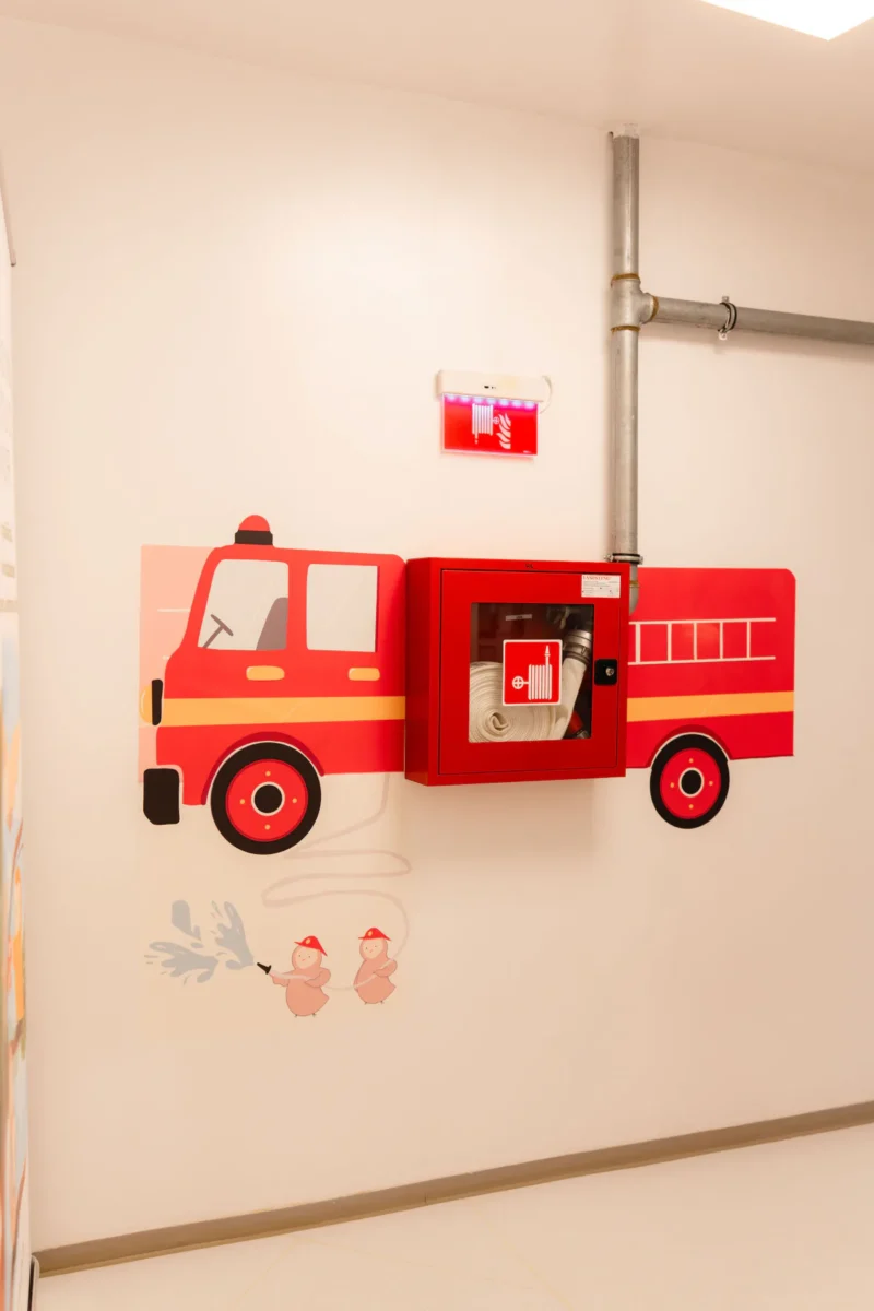 Stingător de incendiu montat într-o carcasă decorativă în formă de mașină de pompieri, pe holul Grădiniței Amicus Junior din Iași